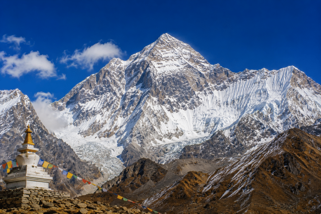 Makalu, the fifth-highest mountain in the world, rising above rugged Himalayan valleys with a Buddhist stupa and prayer flags in the foreground.