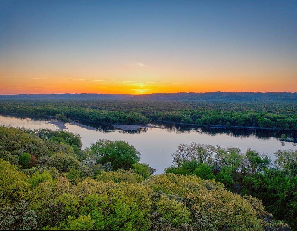 A breathtaking sunrise view over the Mississippi River with lush green trees and a golden horizon.