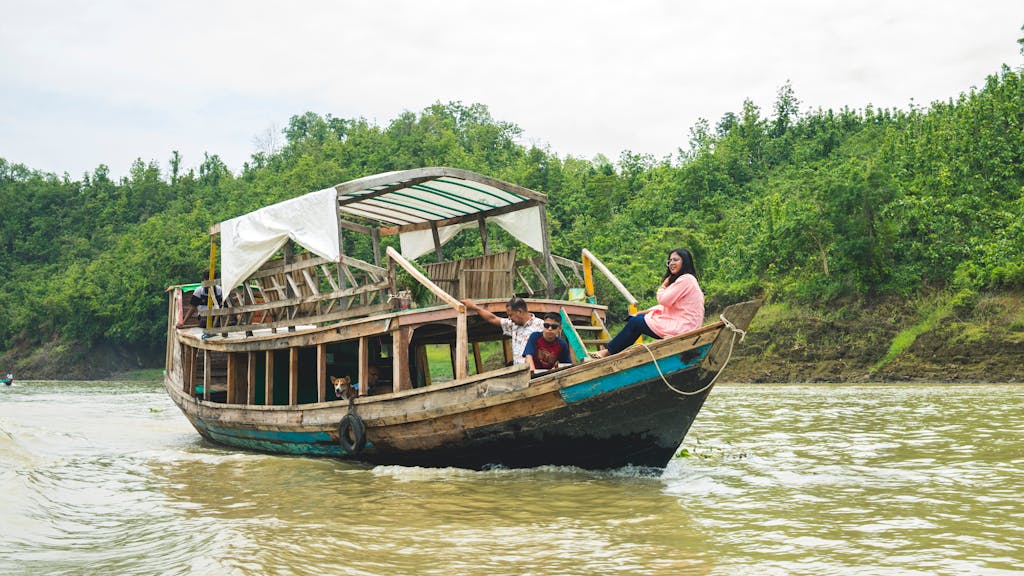 A traditional wooden boat navigates a lush river with passengers enjoying the scenic view.