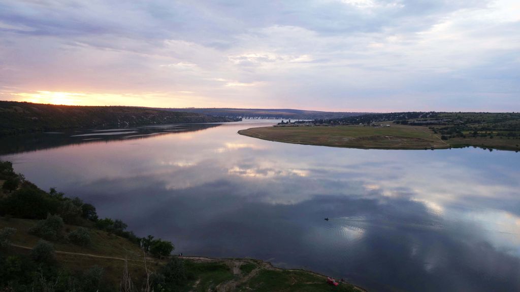Beautiful sunset reflecting on the Dniester River near Roghi, Moldova, with calm waters and lush surroundings.
