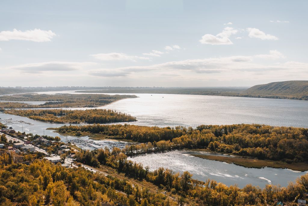 Stunning aerial view of a calm river and lush green islands in autumn, under a clear sky.