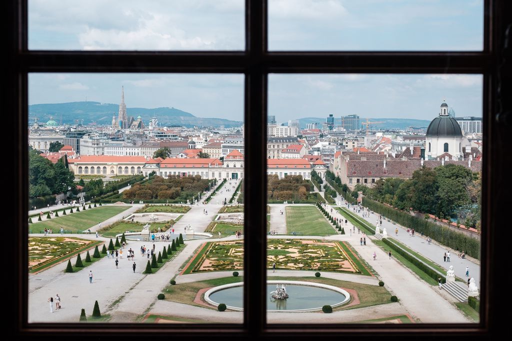 A breathtaking view of Vienna's Belvedere Palace gardens from a window, showcasing baroque architecture and urban landscape.