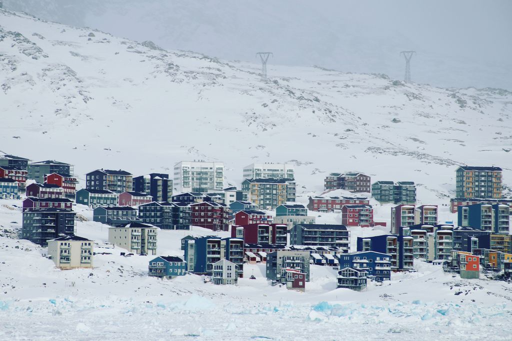 A vibrant, snowy village in Greenland with colorful houses against a mountainous backdrop.