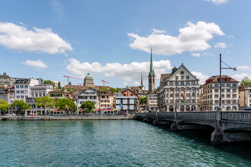 Charming view of Zurich with historic buildings along the Limmat River under a clear blue sky.