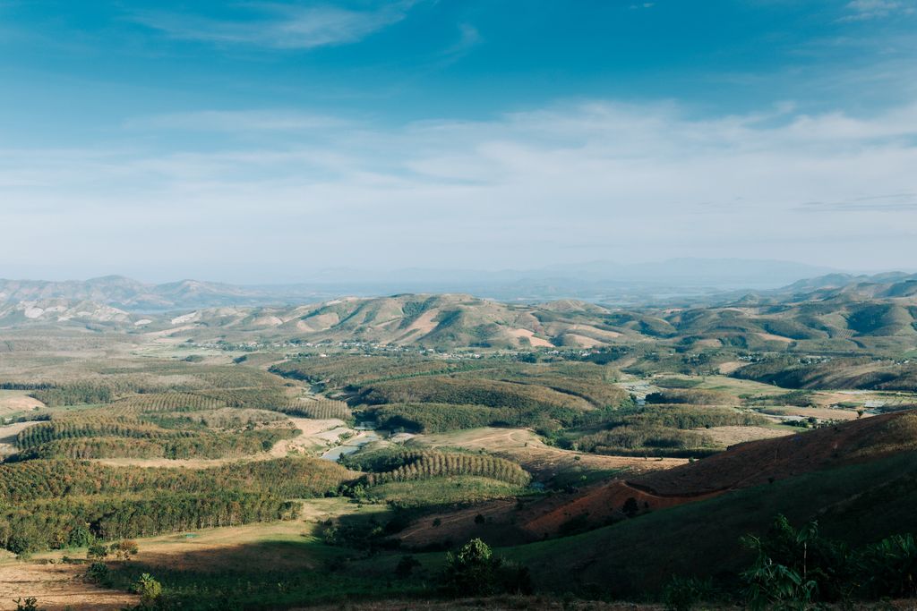 Expansive aerial view of Kon Tum's rolling hills and lush valleys under a clear blue sky.