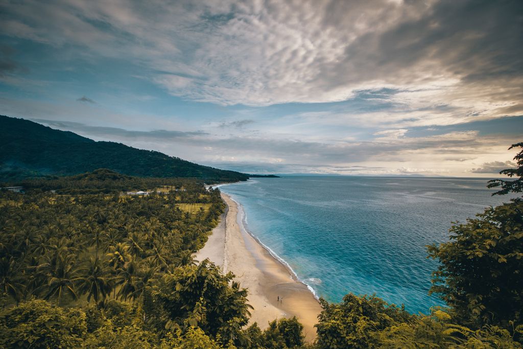 Stunning aerial view of a tranquil coastline in Nusa Tenggara, Indonesia, showcasing lush greenery and sandy beaches.